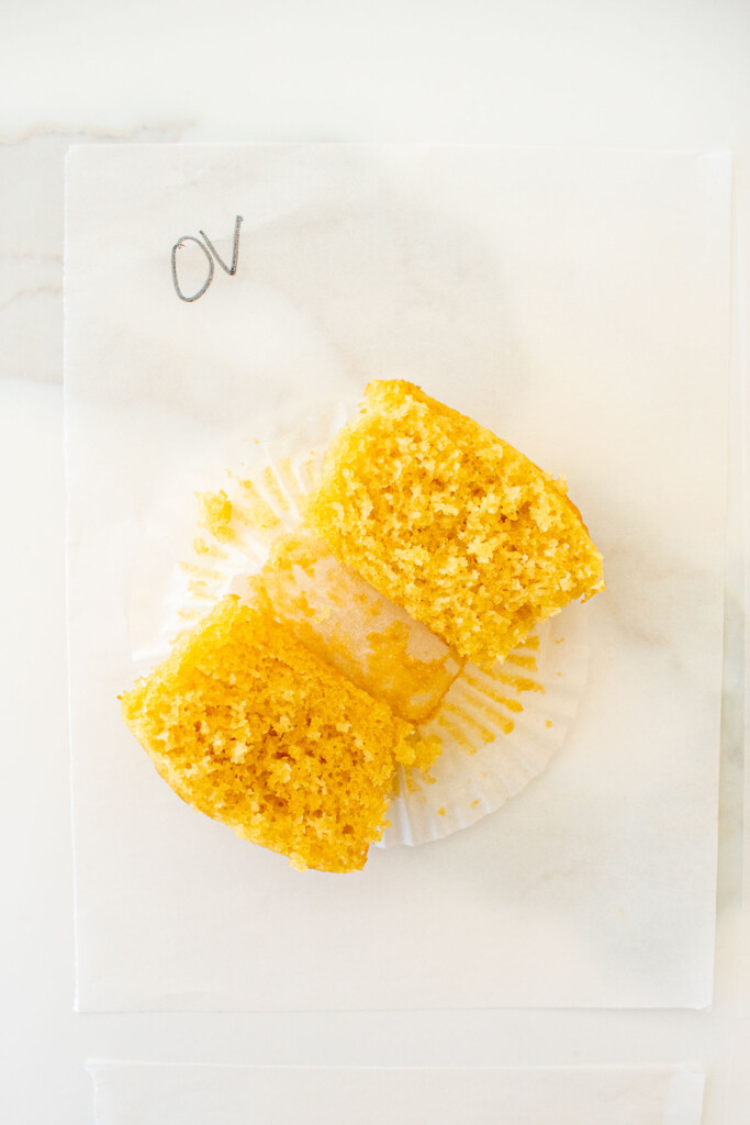 vanilla cupcake cut in half on a piece of parchment paper on a white marble counter made with organic valley butter.