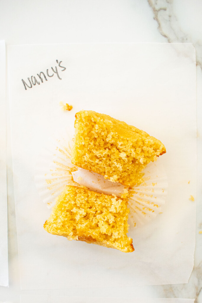 vanilla cupcake cut in half on a white piece of parchment paper on a marble counter with the butter name used written in black marker.