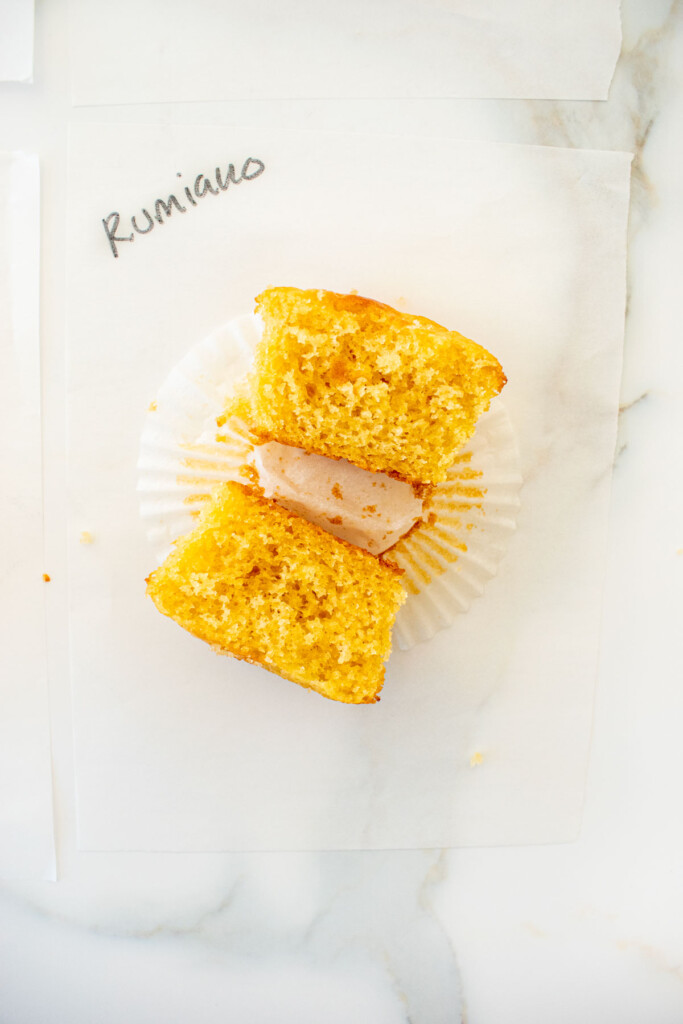 vanilla cupcake cut in half on a white piece of parchment paper on a marble counter with the butter name used written in black marker.