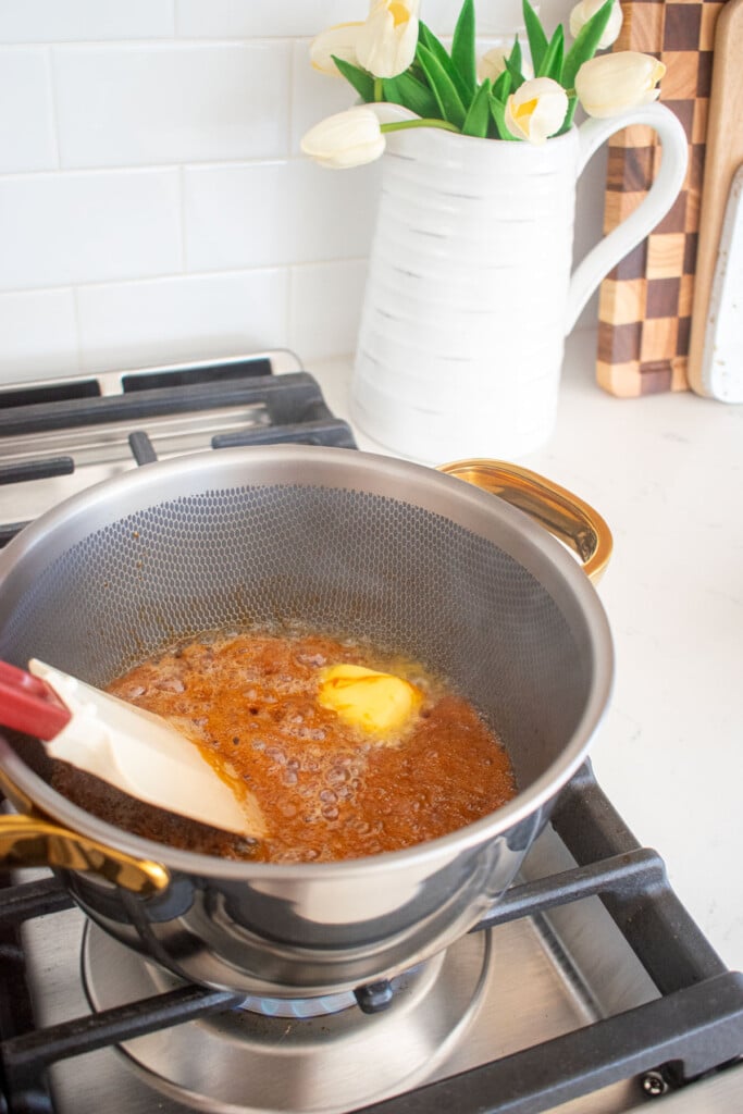 butter being stirred into homemade caramel sauce on the stovetop in a titanium pot.