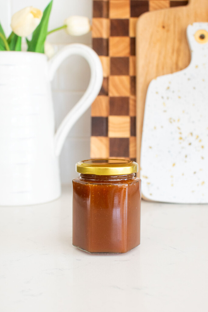 homemade caramel sauce with bone broth in a glass jar on a white marble counter.