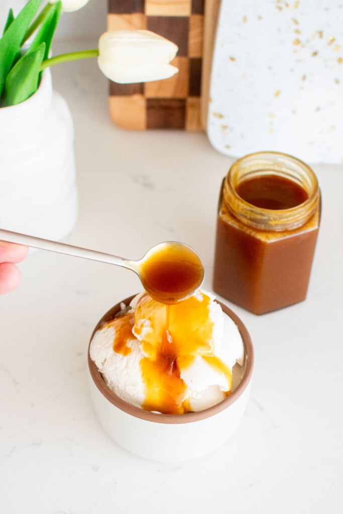 homemade caramel sauce with bone broth being spooned onto vanilla ice cream on a white marble counter.