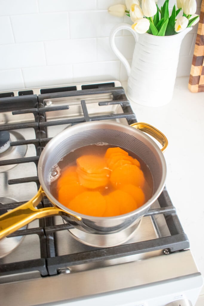 sweet potato slices in a pot on the stovetop boiling.