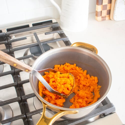 mashed sweet potato in a pot on the stovetop with a potato masher.