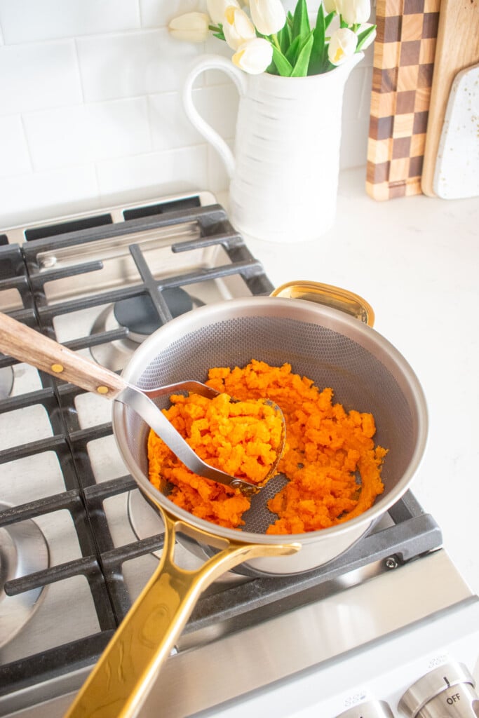 mashed sweet potato in a pot on the stovetop with a potato masher.