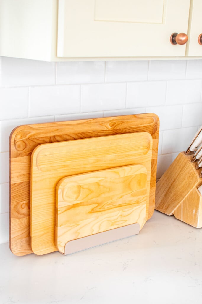 set of caraway wood cutting board in a holder on a white marble kitchen counter.