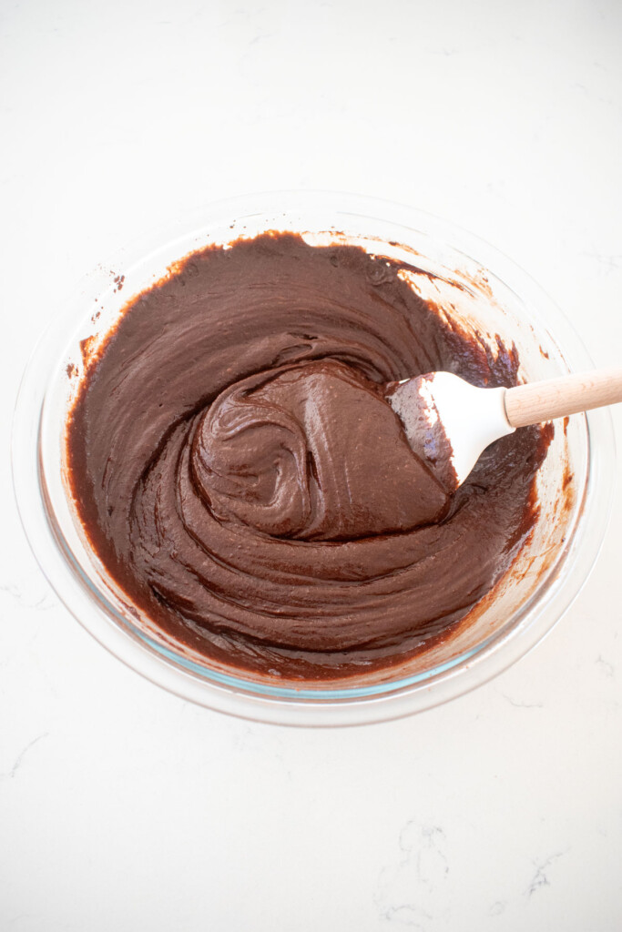 eggless chocolate cake batter mixed together in a glass mixing bowl on a white marble counter.