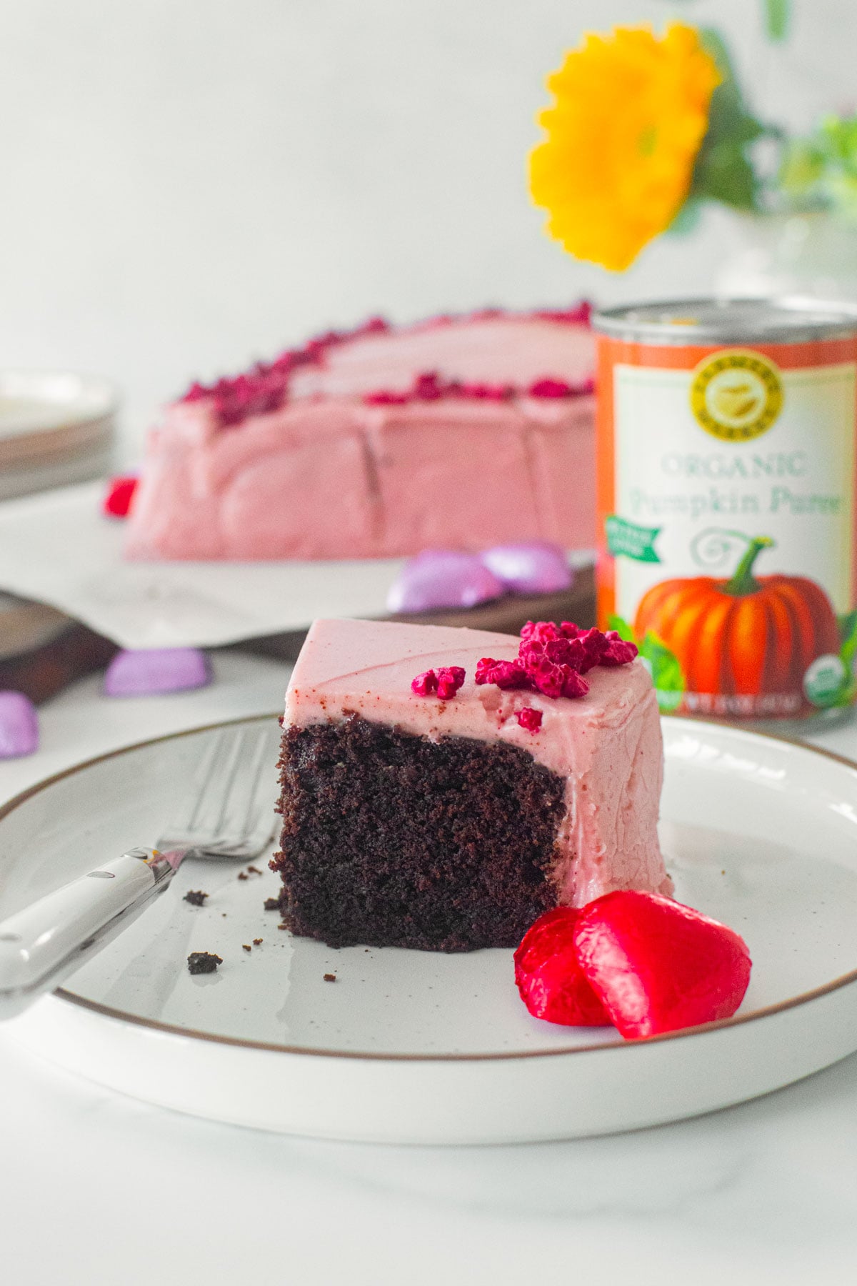 slice of eggless chocolate heart cake with pink frosting on a plate on a white marble counter.