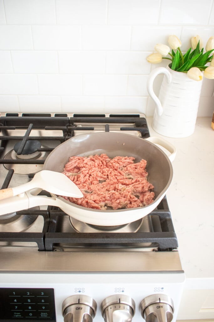 large skillet on the stovetop with olive oil and raw ground turkey.