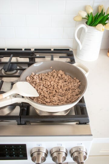 large skillet on the stovetop with ground turkey being cooked.