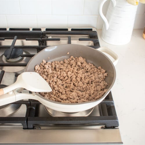 large skillet on the stovetop with ground turkey being cooked.