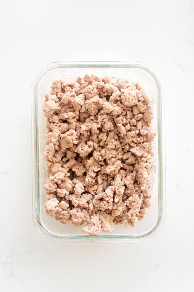 cooked ground turkey in a glass tupperware on a marble counter.