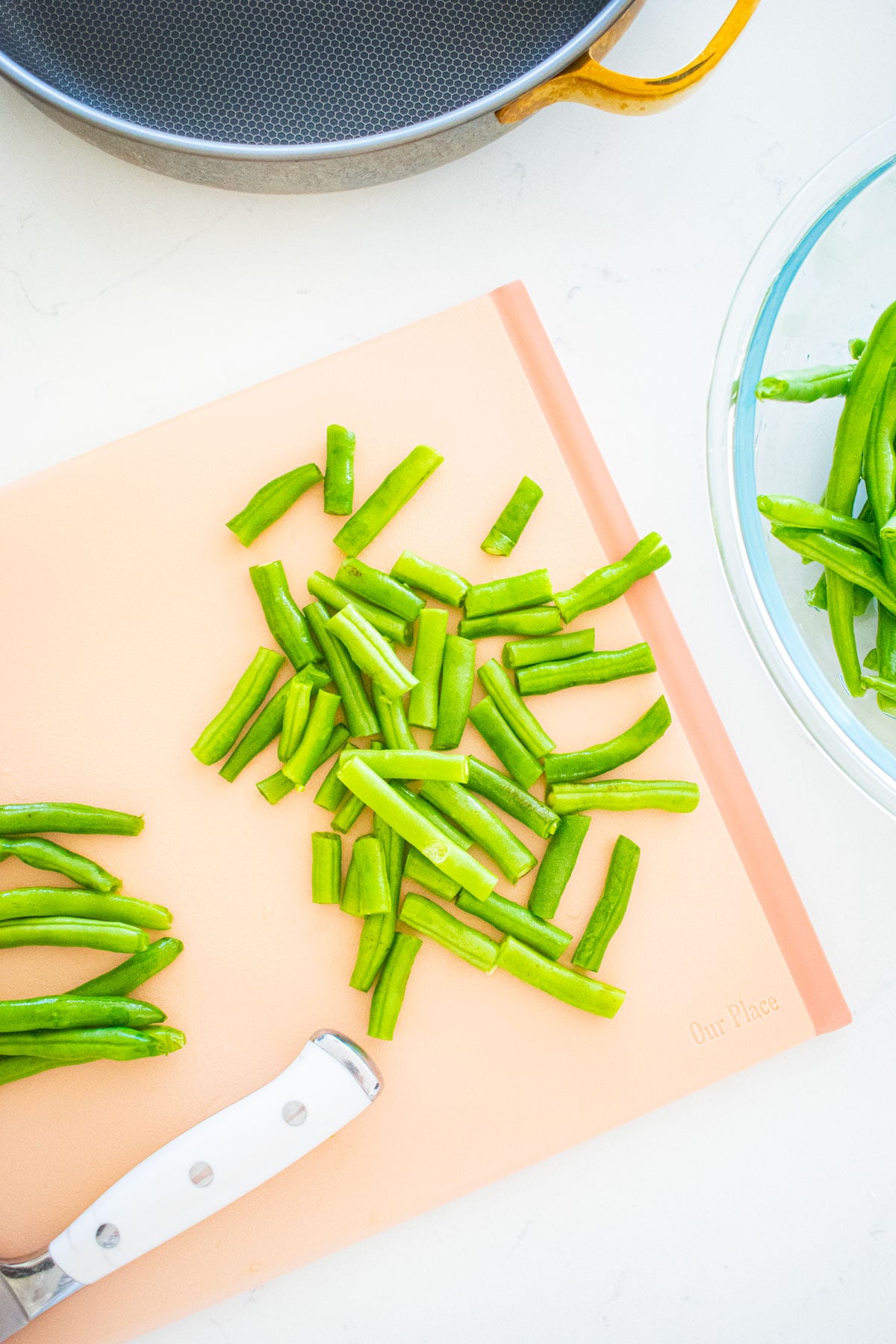 our place cutting board with green beans being cut on a white marble counter.