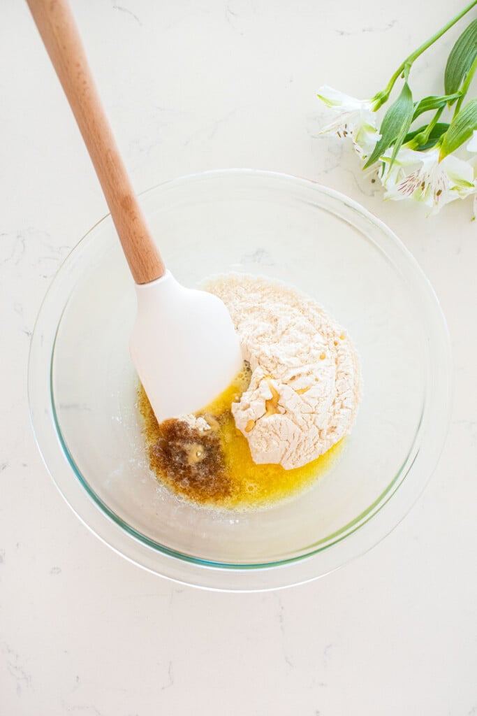 ingredients for streusel topping in a glass mixing bowl on a white marble counter with a spatula in the bowl.