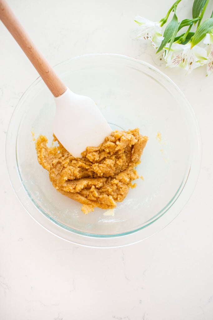 streusel topping in a glass mixing bowl with a spatula on a white marble counter.