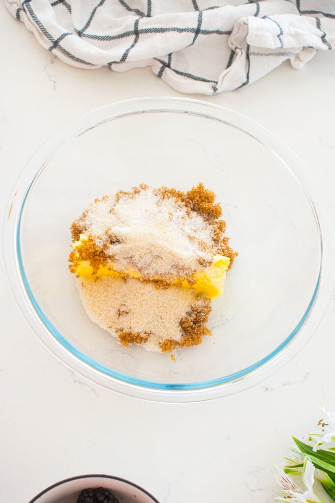 butter and sugar in a glass mixing bowl on a white marble counter.