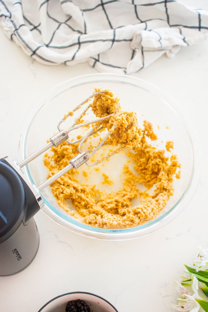 creamed butter and sugar in a glass mixing bowl on a white marble counter.