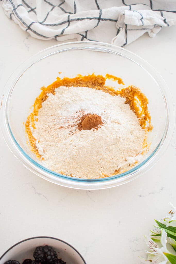 ingredients for sweet potato muffins in a glass mixing bowl on a white marble counter.
