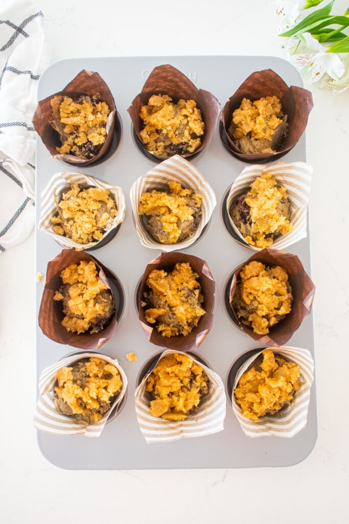blackberry sweet potato muffin batter in a muffin pan with streusel topping on a white marble counter.