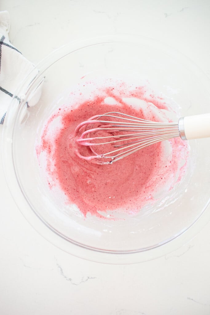 blackberry glaze in a glass mixing with a whisk on a white marble counter.