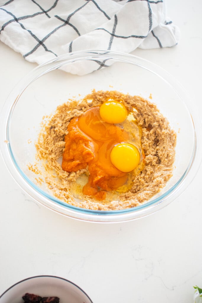 eggs and sweet potato puree in a glass mixing bowl with creamed butter and sugar on a white marble counter.