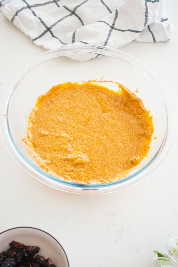 mixed wet ingredients for sweet potato muffins in a glass mixing bowl on a white marble counter.