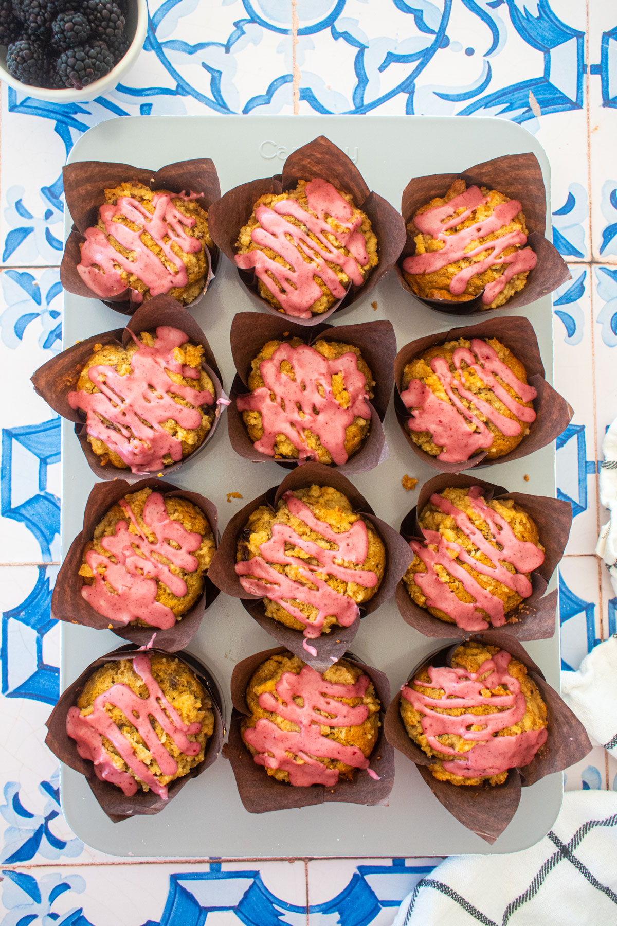 blackberry sweet potato muffins with blackberry glaze in a muffin pan on a blue tile table.
