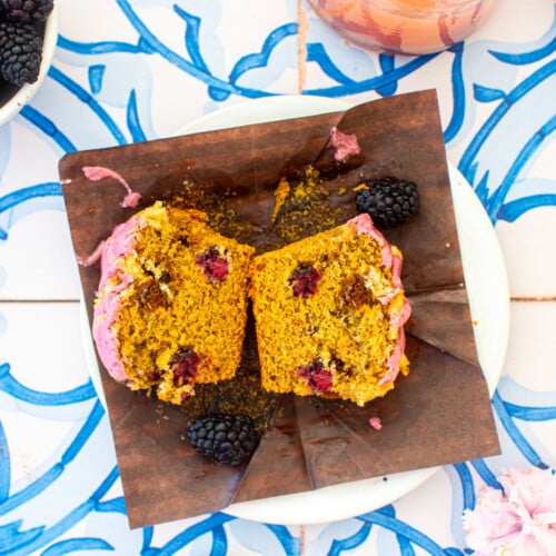 blackberry sweet potato muffin cut in half on a plate on a blue tile table with pink lemonade.