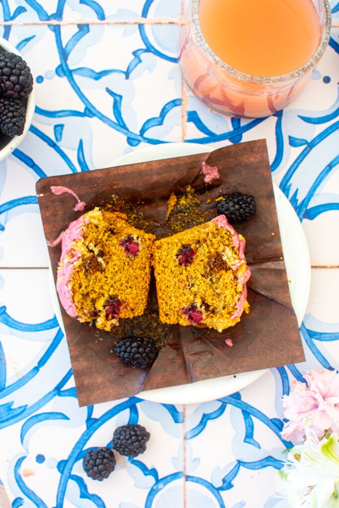 blackberry sweet potato muffin cut in half on a plate on a blue tile table with pink lemonade.