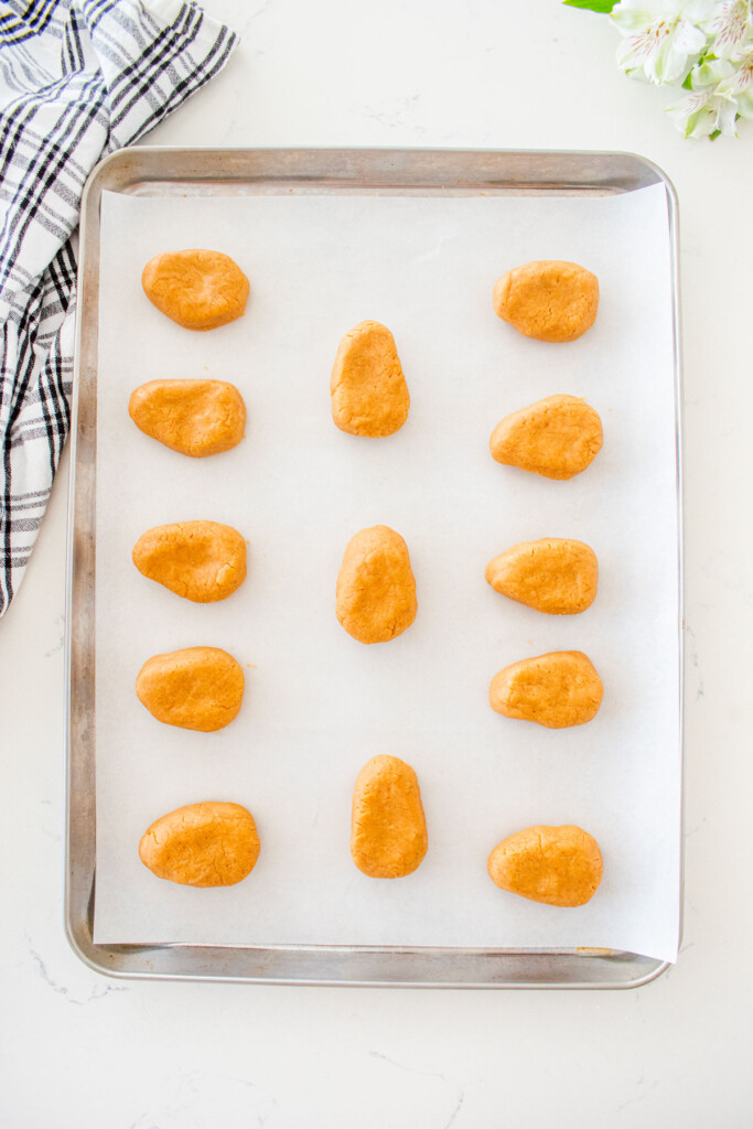 baking sheet with parchment paper and peanut butter filling formed into eggs on a white marble counter.