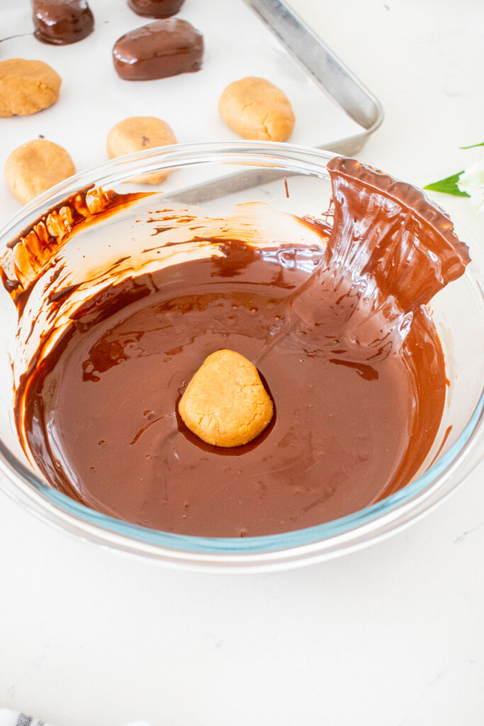peanut butter egg in a bowl of melted dark chocolate on a white marble counter.