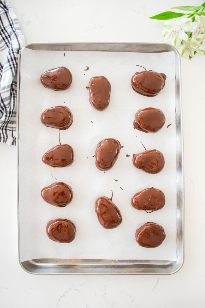 chocolate dipped peanut butter eggs on a baking sheet on a white marble counter.