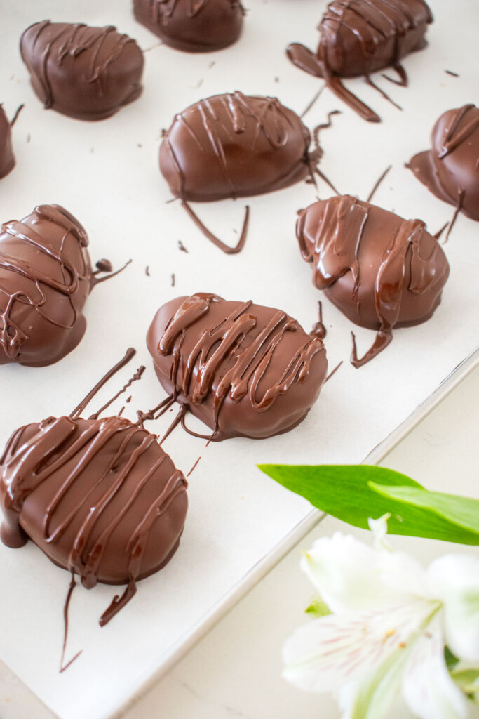 chocolate peanut butter eggs with chocolate drizzle on top on a baking sheet on a white marble counter.