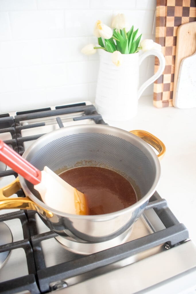 saucepan on the stovetop with melted cane sugar being stirred with a spatula.