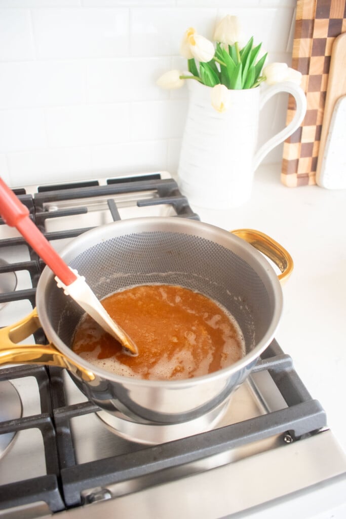 butter being added into melted cane sugar in a saucepan on the stovetop being stirred with a spatula.