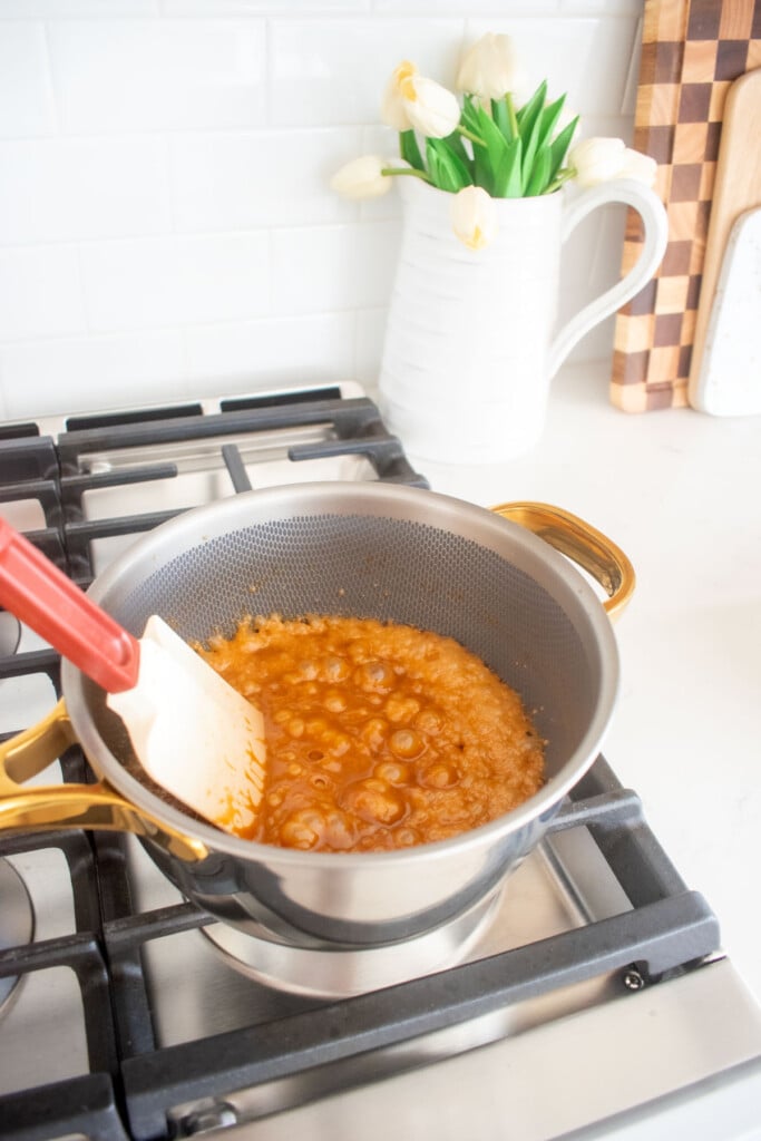cream being stirred into caramel in a saucepan on the stovetop.