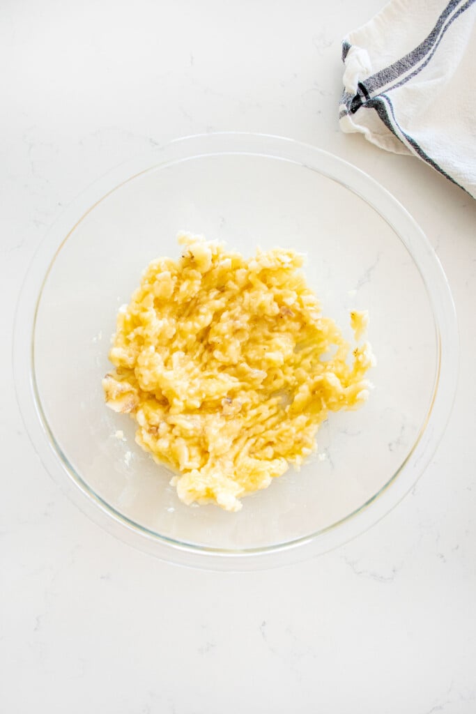 glass mixing bowl with mashed bananas on a white marble counter.