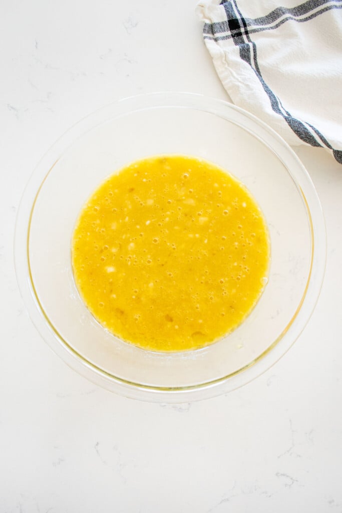 wet ingredients for banana dog cake in a glass mixing bowl on a marble counter.