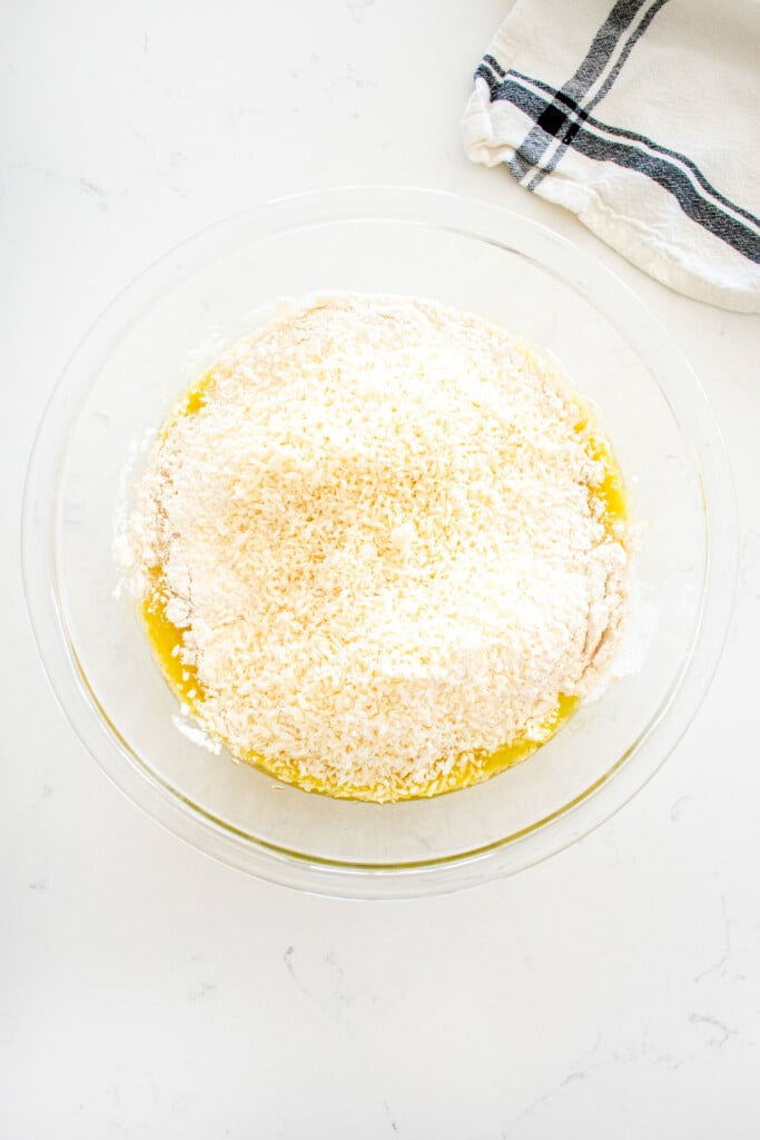 dry ingredients added to wet ingredients for a banana dog cake batter in a glass mixing bowl on a marble counter.