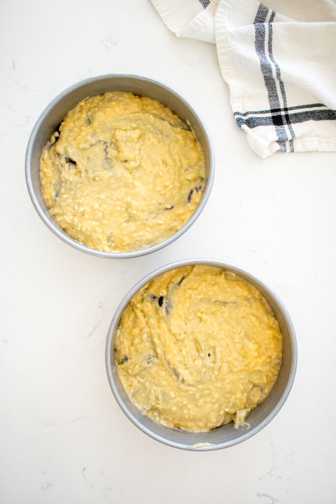 two 6-inch cake pans with dog birthday cake batter on a marble counter.