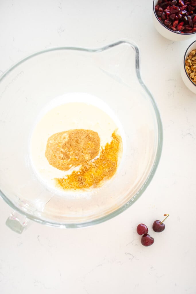 glass mixing bowl with heavy whipping cream and vanilla on a marble counter.