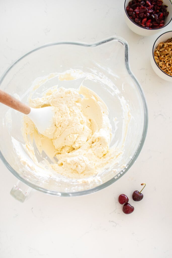 glass mixing bowl with whipped cream with a spatula in it on a marble counter.
