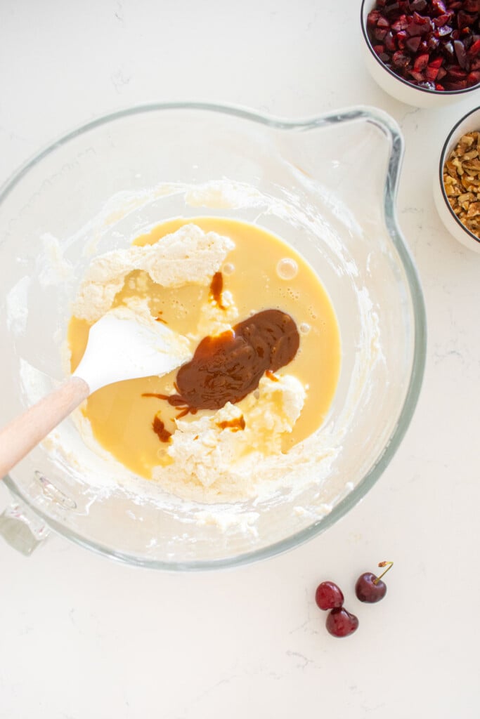 homemade whipped cream in a glass mixing bowl with sweetened condensed milk and caramel sauce added to it with a spatula.