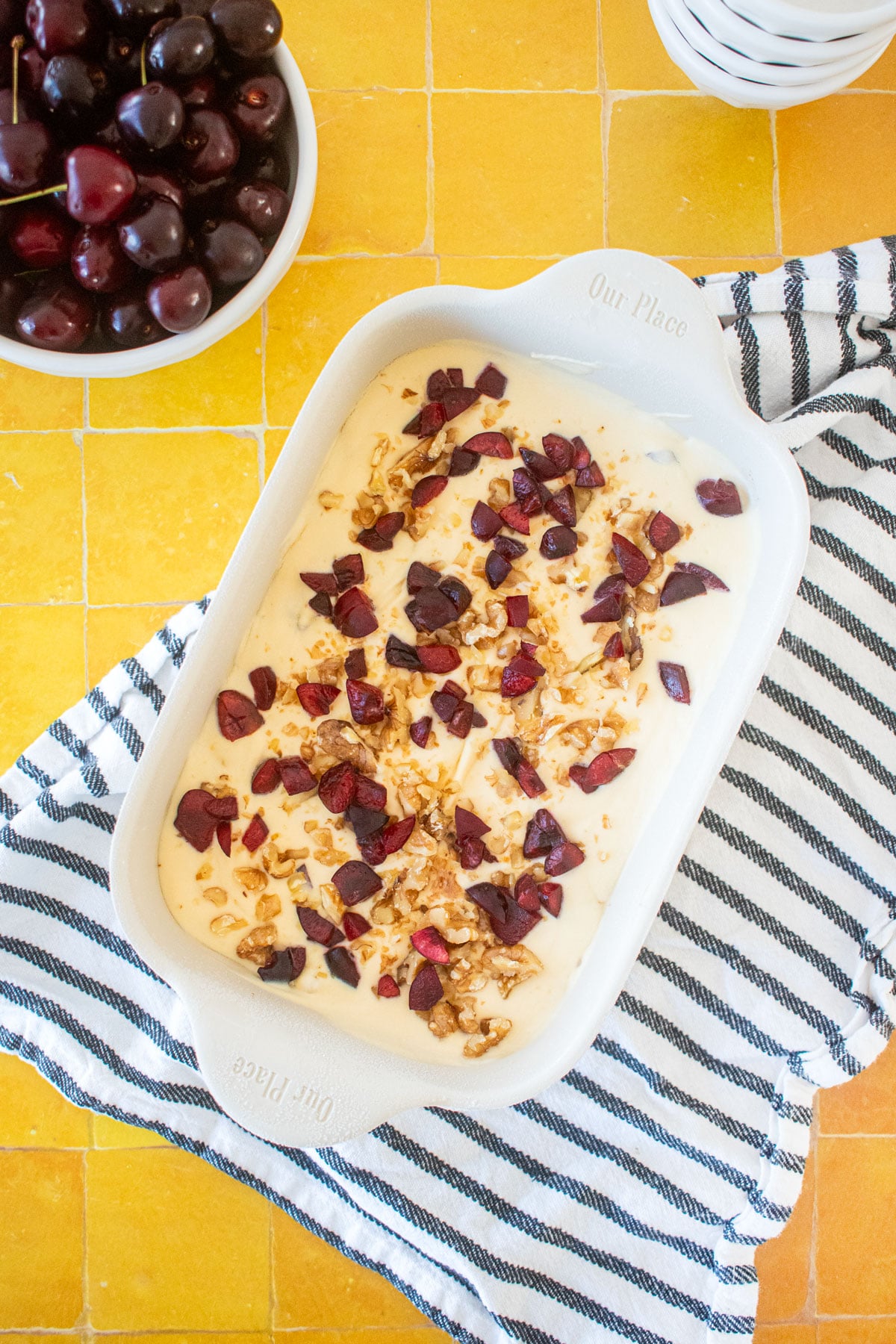 frozen palmer house ice cream in a baking dish on a yellow tile table with a bowl of cherries and ice cream dishes.