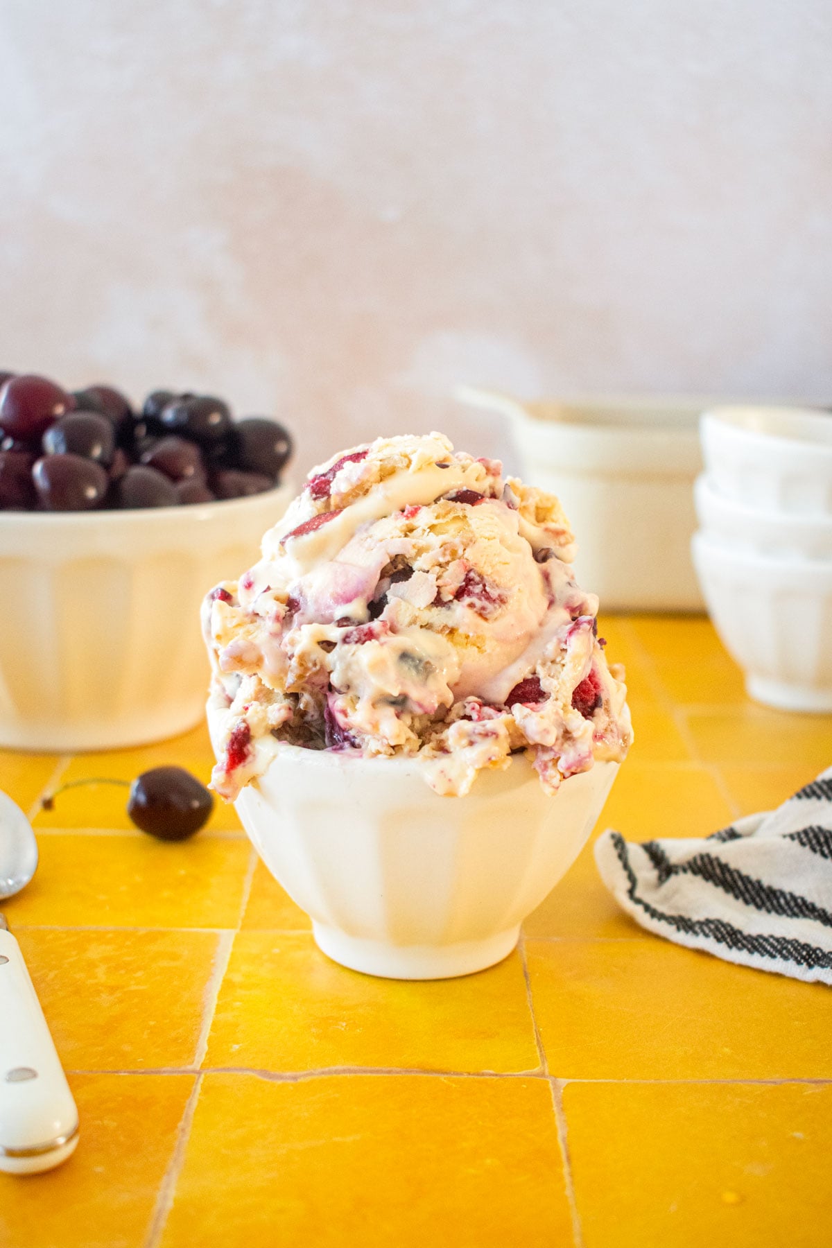 palmer house ice cream scooped high in a small ice cream dish on a yellow tile table with a bowl of cherries in the background.