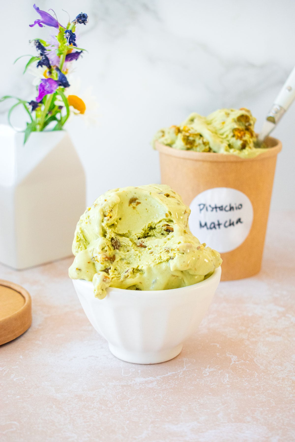 ice cream dish with scoops of pistachio matcha no churn ice cream with a bite taken out on a table with a small vase of fresh flowers.