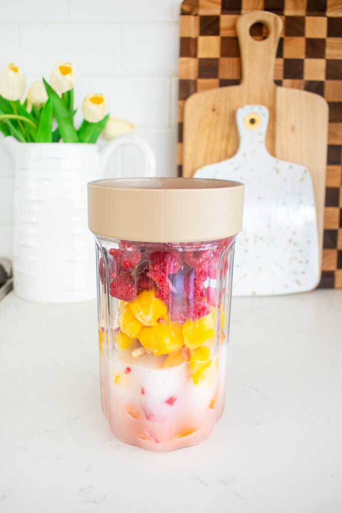 blender bottle with frozen fruit ingredients for raspberry apricot smoothie on a marble counter.