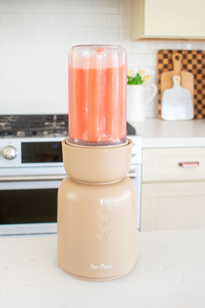 blender with raspberry apricot smoothie being blended on a marble countertop.