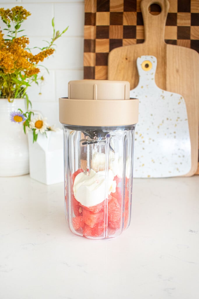 smoothie blender with greek yogurt and watermelon in it on a marble counter.