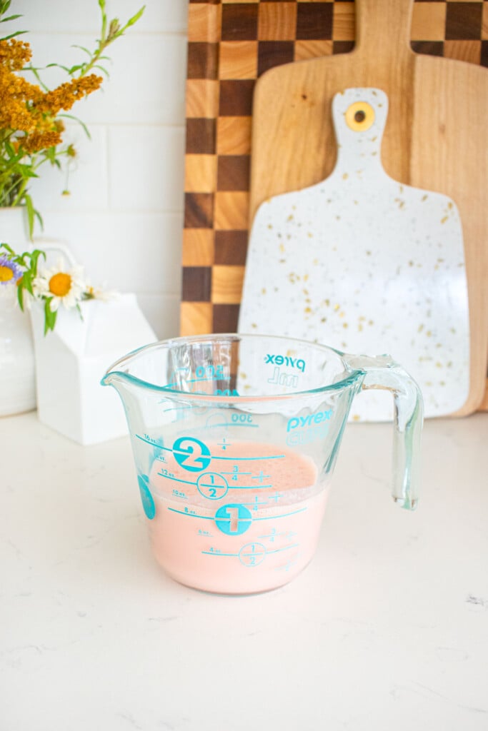 blended greek yogurt and watermelon liquid in a liquid measuring cup on a marble counter.